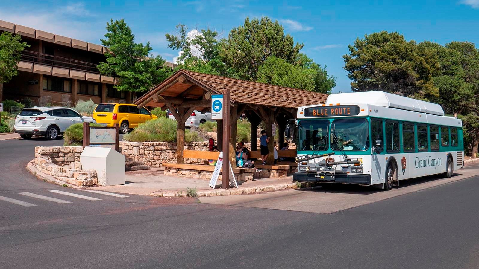 Several people within a rustic, open air shelter, about to board a white and green bus 