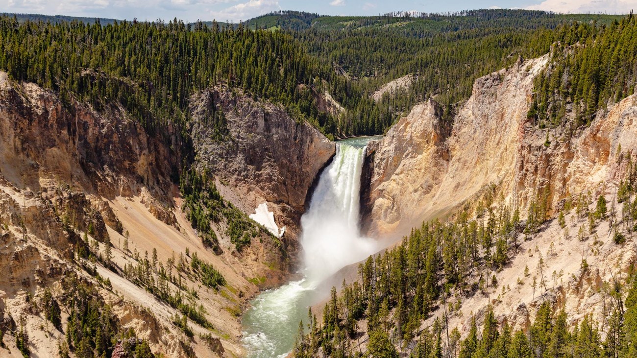 A waterfall cascades over a cliff in a canyon with pale colored walls.