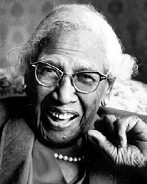 Black and white photo of woman sitting in a chair, smiling. 