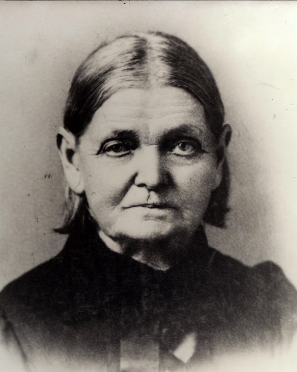 A middle aged woman makes a serious face for the camera in an 1800s portrait photo.