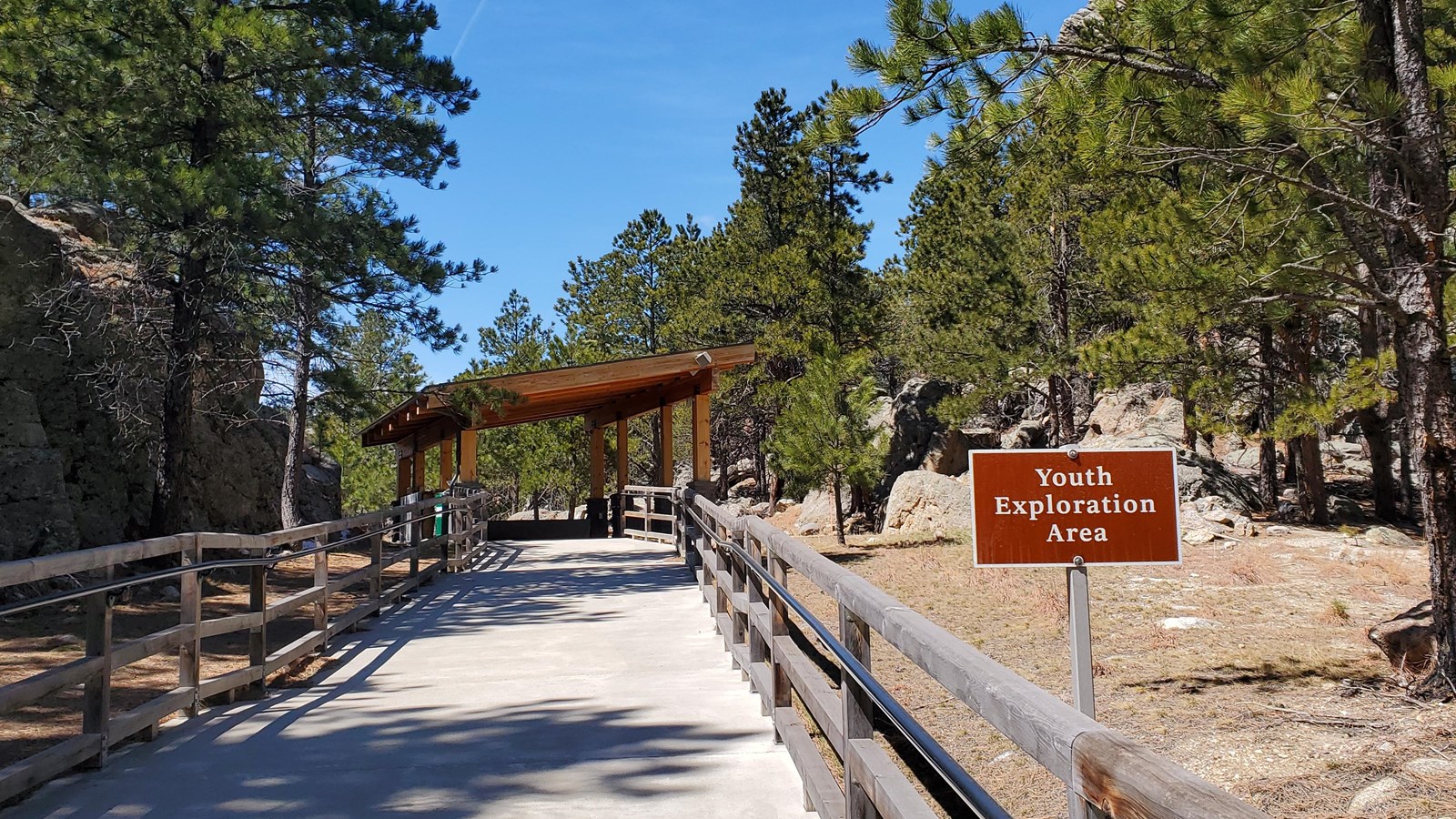 Paved path leading up to a wooden covered structure and surrounded by trees