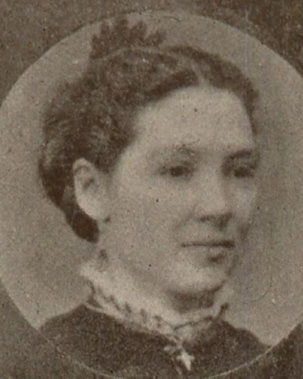 An image of a woman with her hair up in a dark shirt with a white collar.