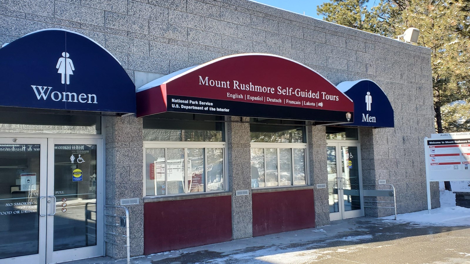A grey building with a red awning above a walk up service window. Two blue awnings on either side.