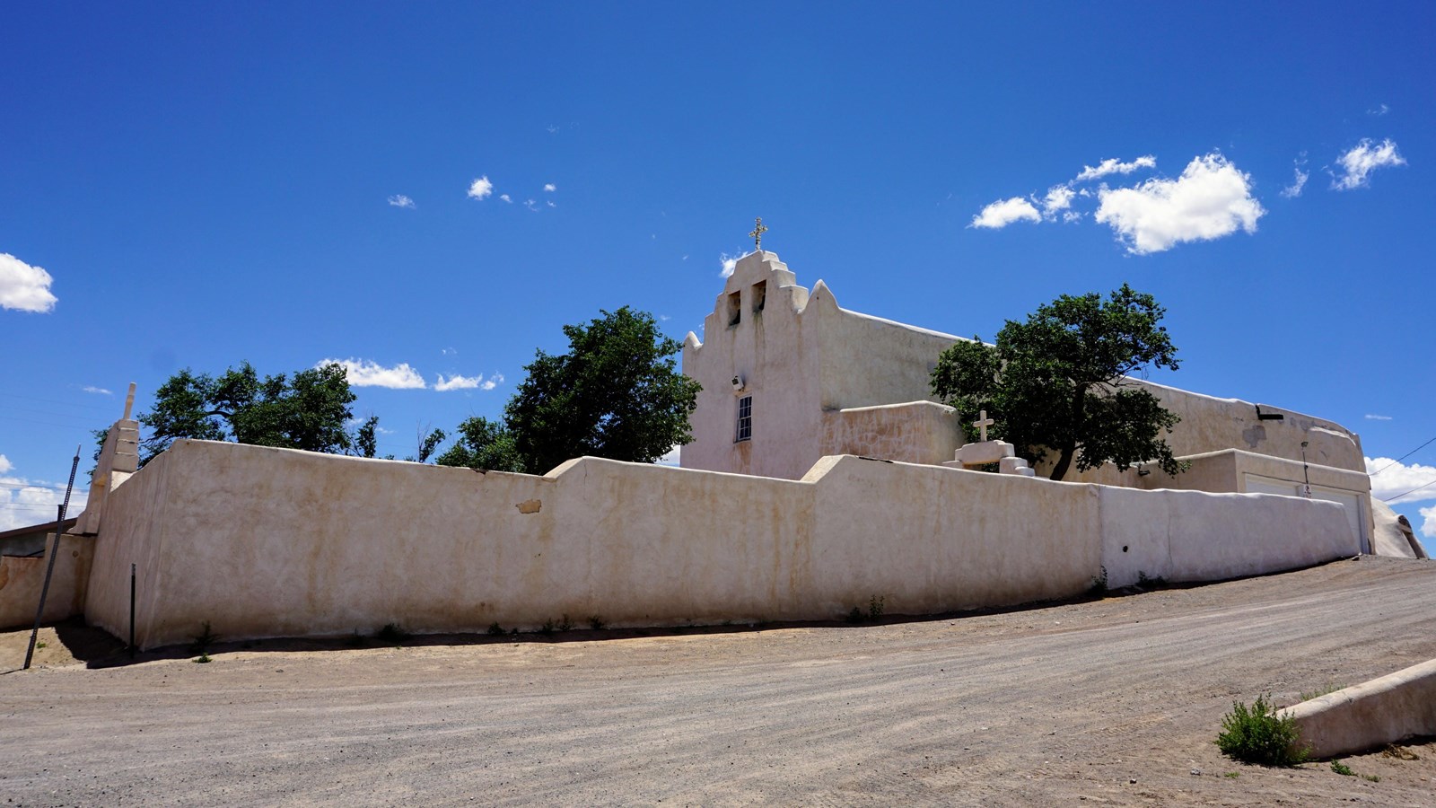 A large white adobe building with a wall surrounding it.