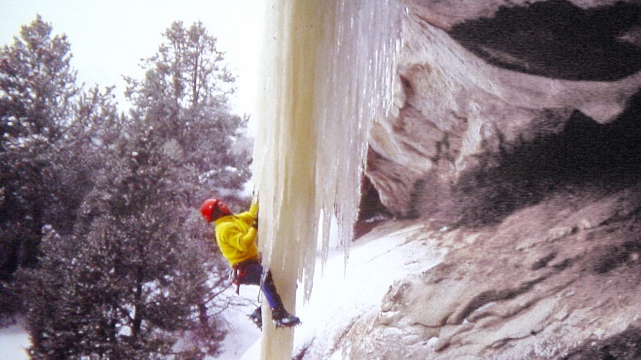 A person climbing an ice formation hanging from the granite.