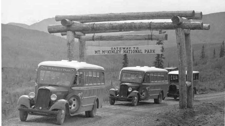 three old buses traveling under an arch bearing a sign: gateway to mckinley national park