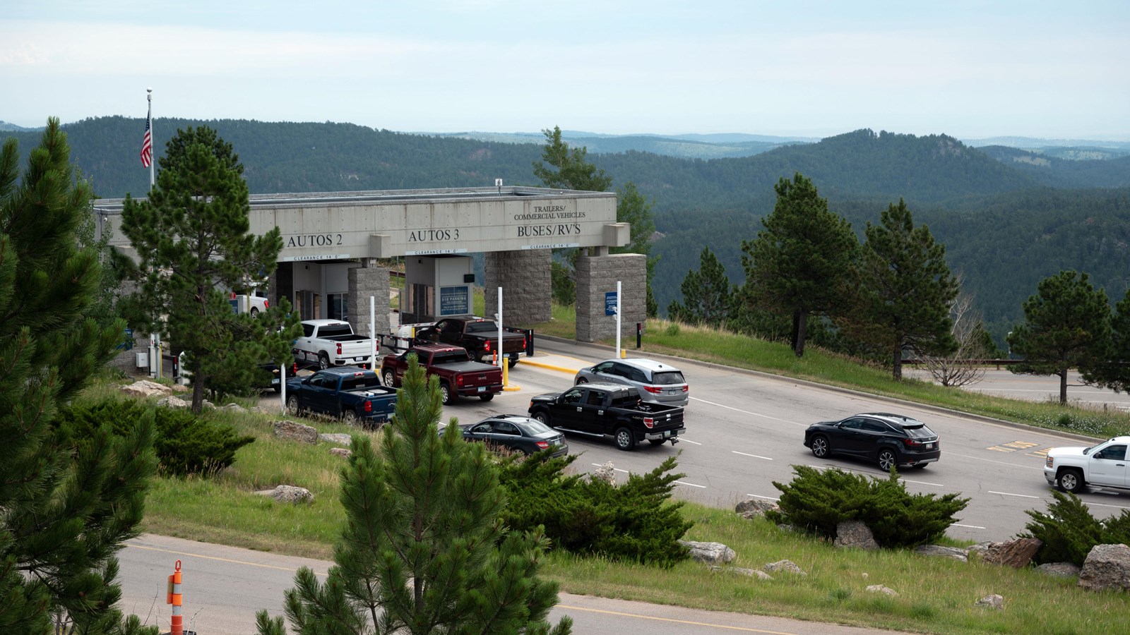Cars lined up on the road in front of a grey entrance gate with 4 lanes.