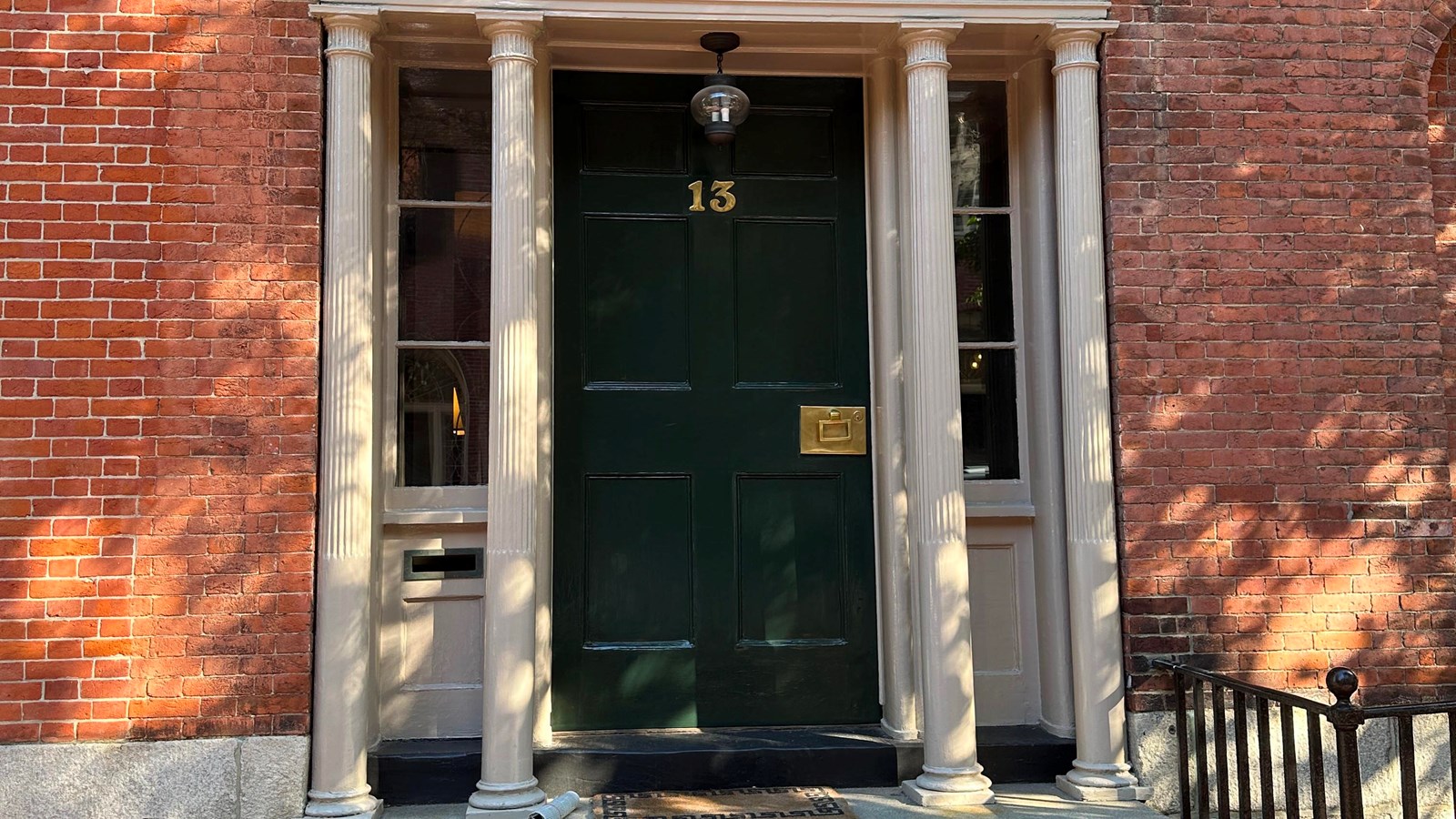 Photo of a brick house with a black door with a big 13 on it. Surround it is a white frame