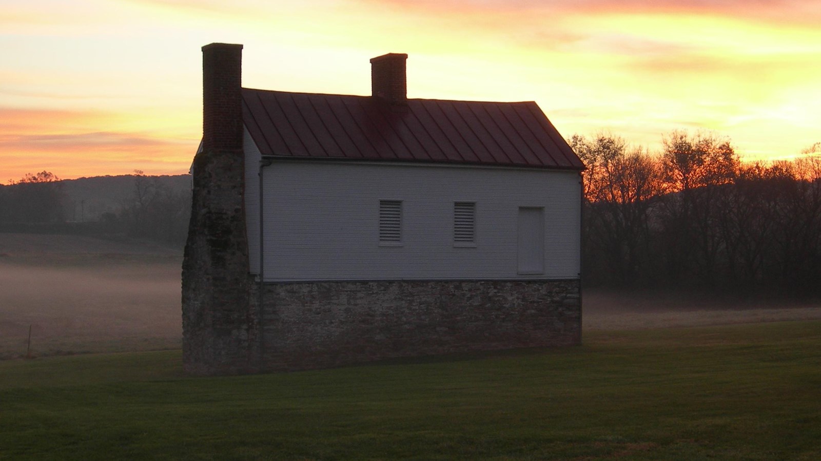 A small, two-story house with stone walls on ground floor and wood siding on the second.