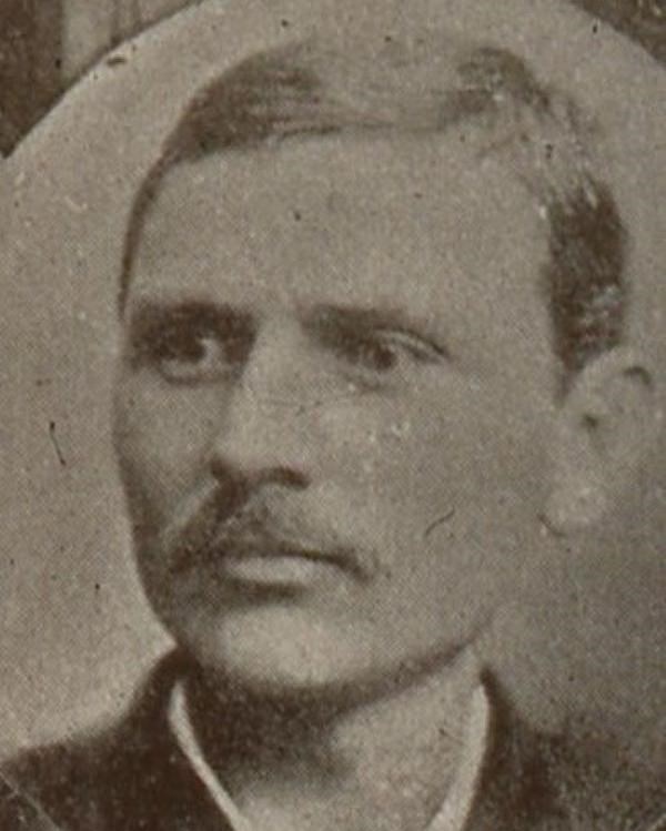 An image of a man with short hair and a black suit jacket with a white shirt underneath.