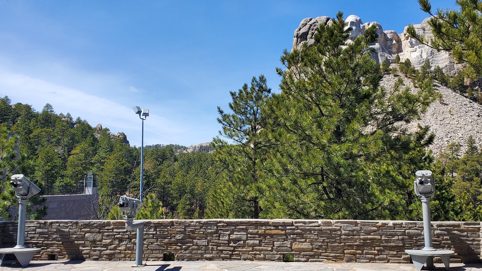 Photo of a grey stone terrace with a short stone wall and three coin operated viewing binoculars.