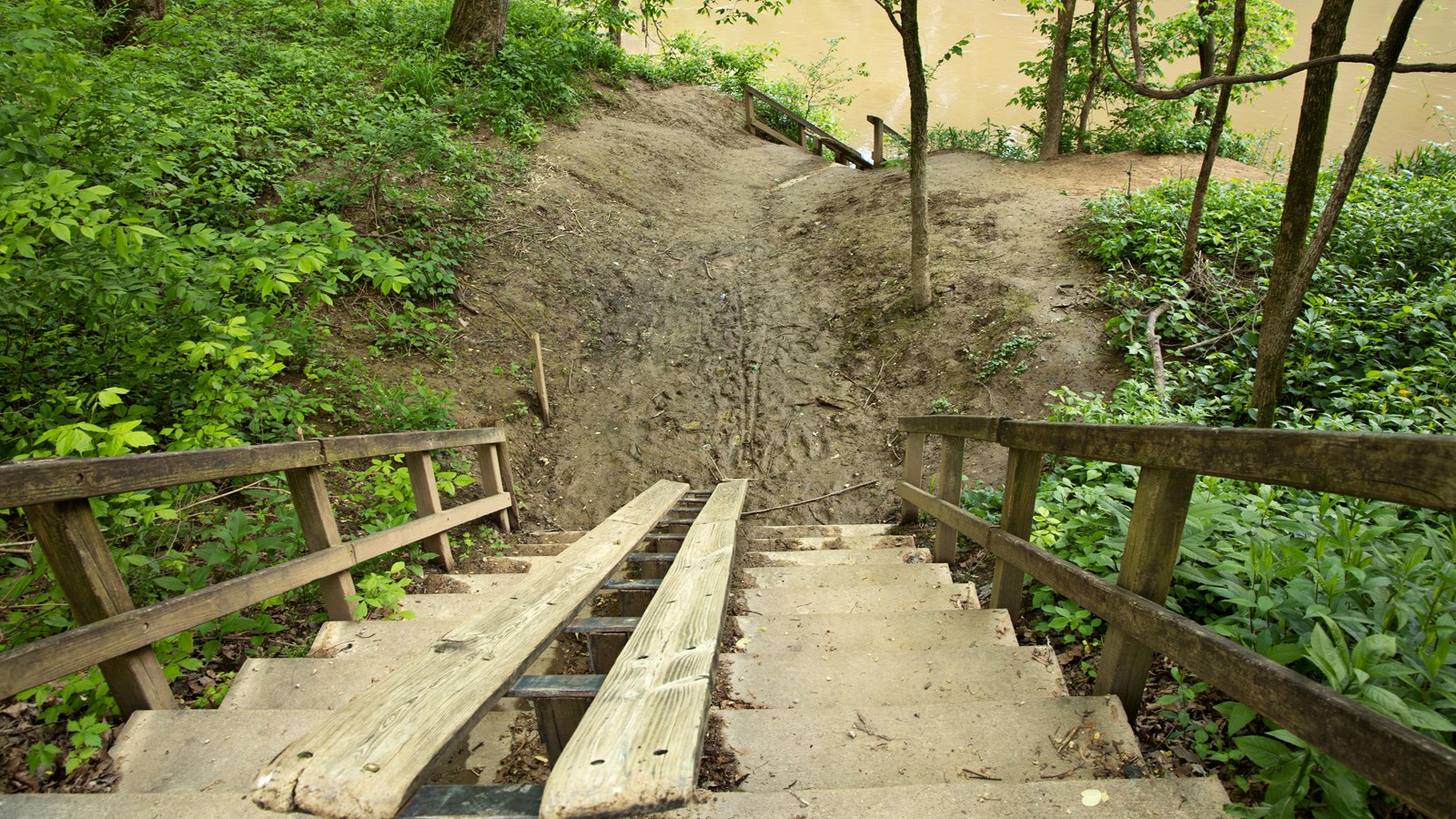A wooden canoe and kayak ramp and concrete steps lead to the river.