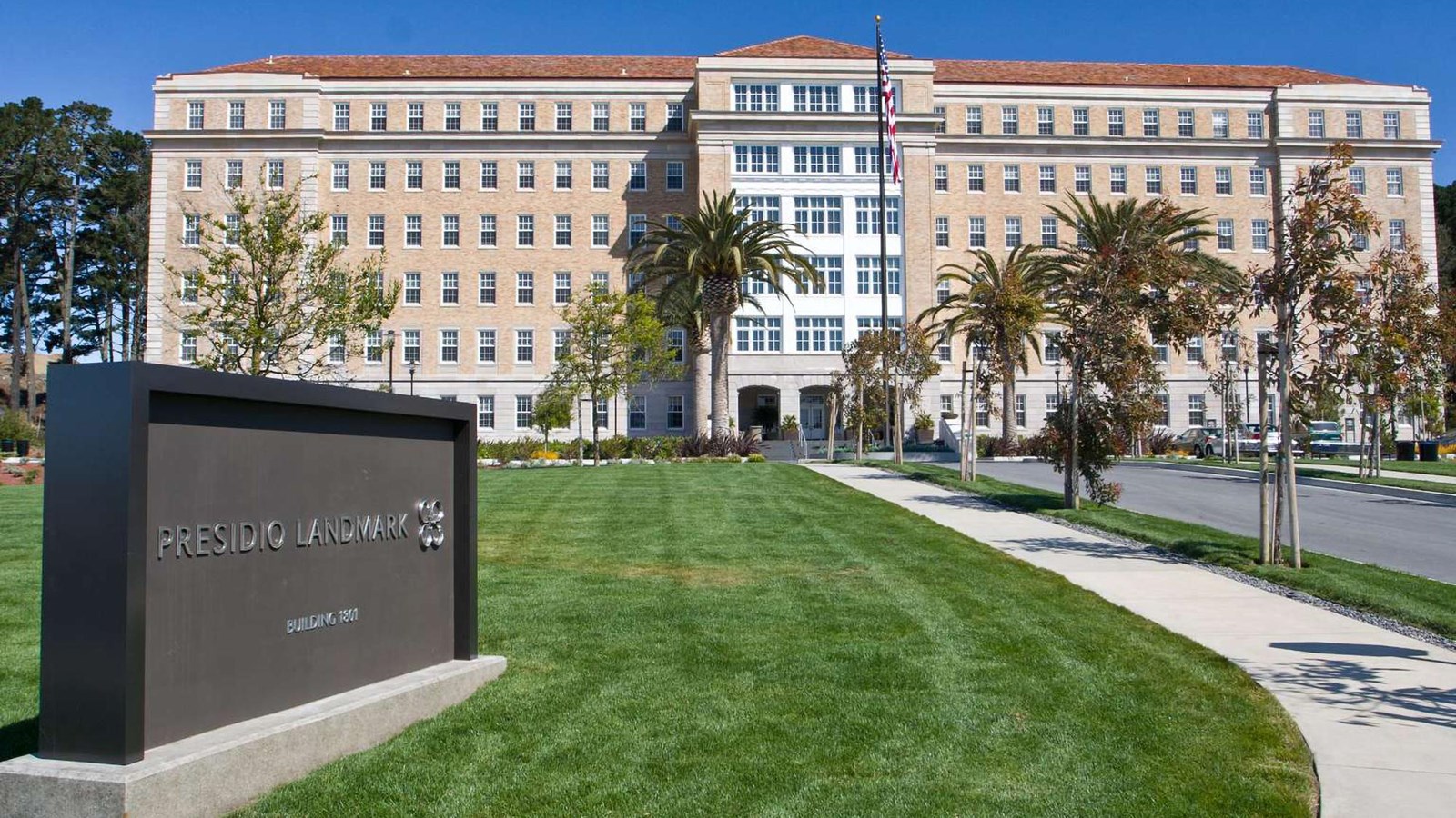 The massive eight story yellow brick Presidio Landmark, with a grassy lawn, sidewalk and sign.