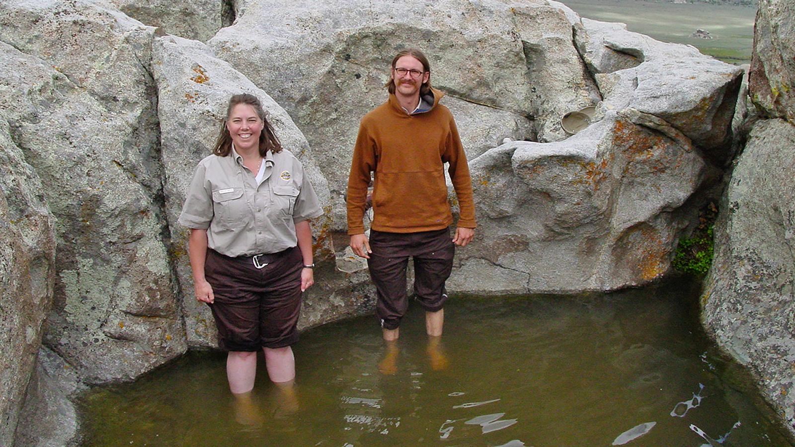Two people with their pant legs rolled up wade in the water in the