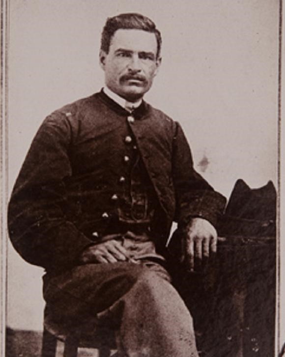 Seated soldier with short hair and mustache. His left arm rests on a table, his right on his lap.