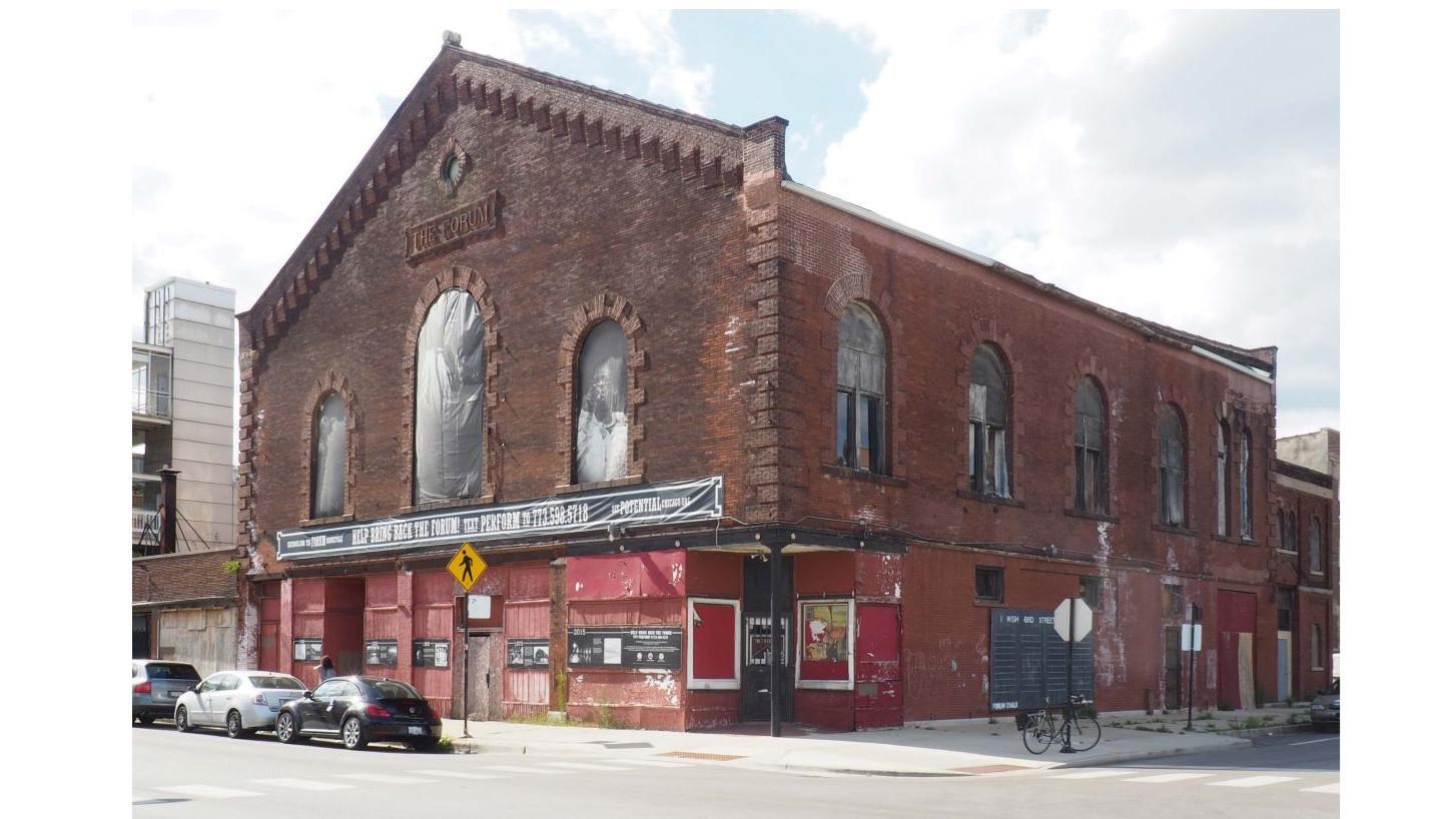 Three story brick building with store front windows and tall arched windows on the upper levels