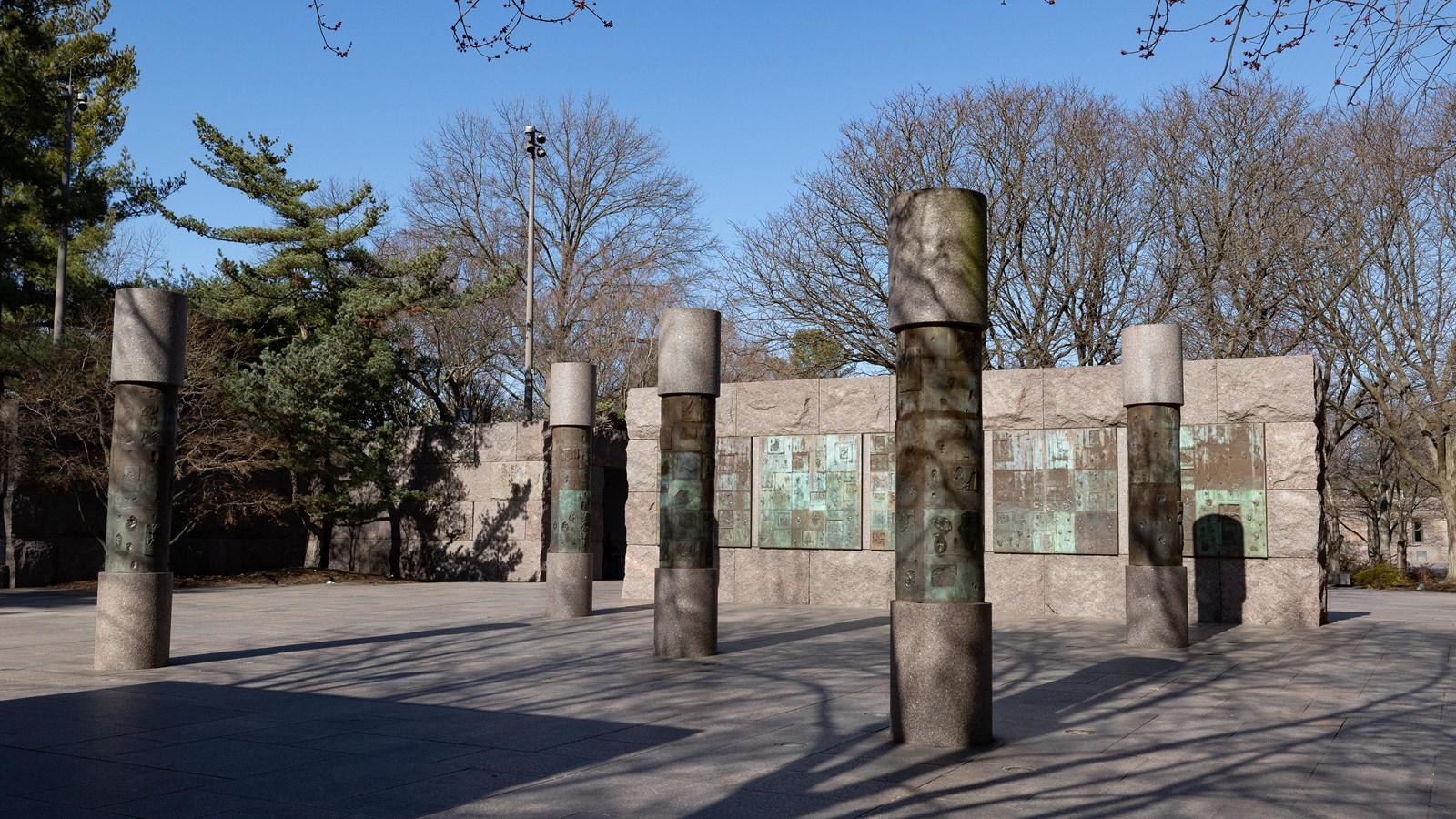 Five columns stand in a pyramid formation in front of a stone wall of similar pattern.
