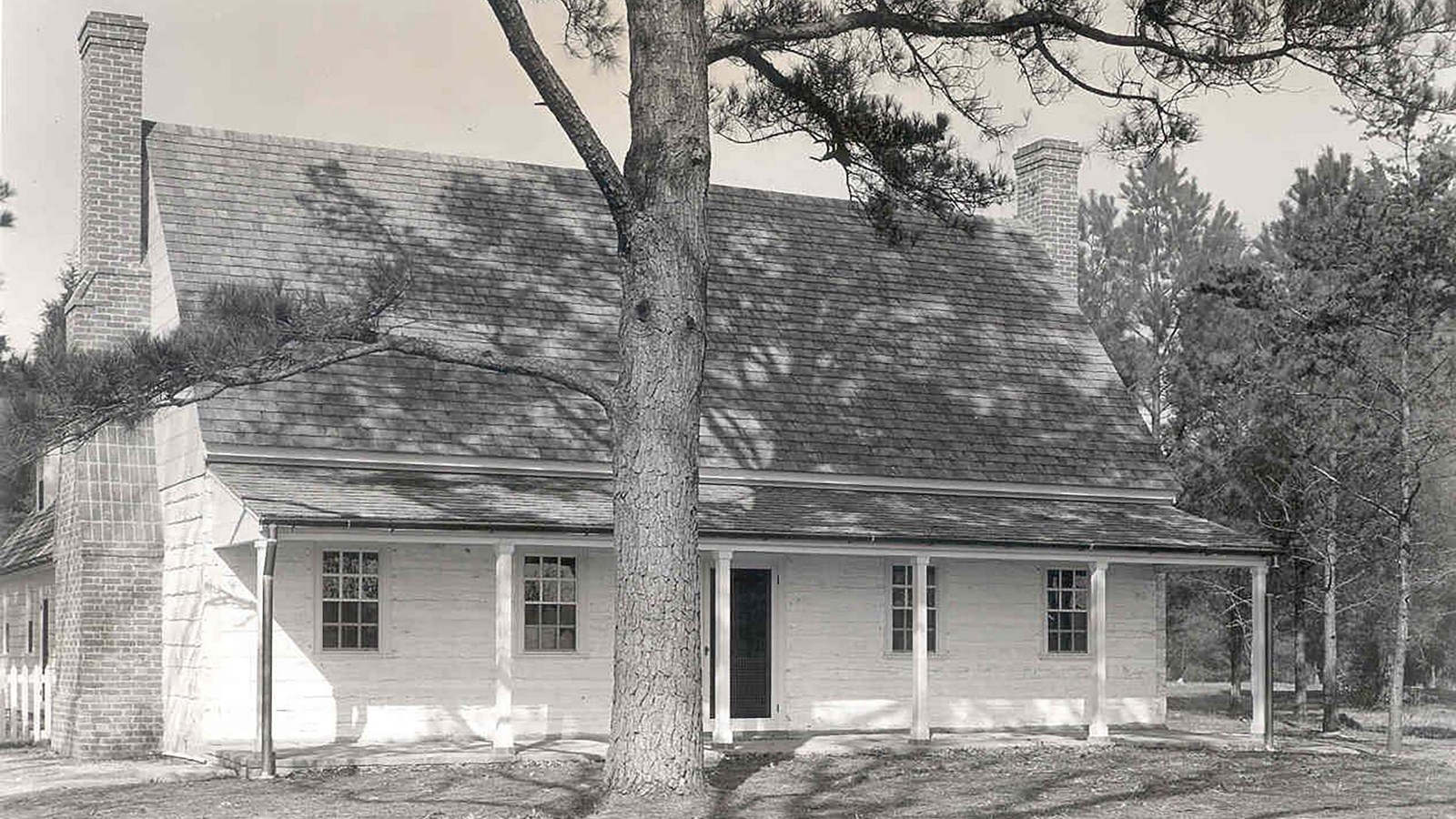 A black and white photo of a house with a tree in the front.