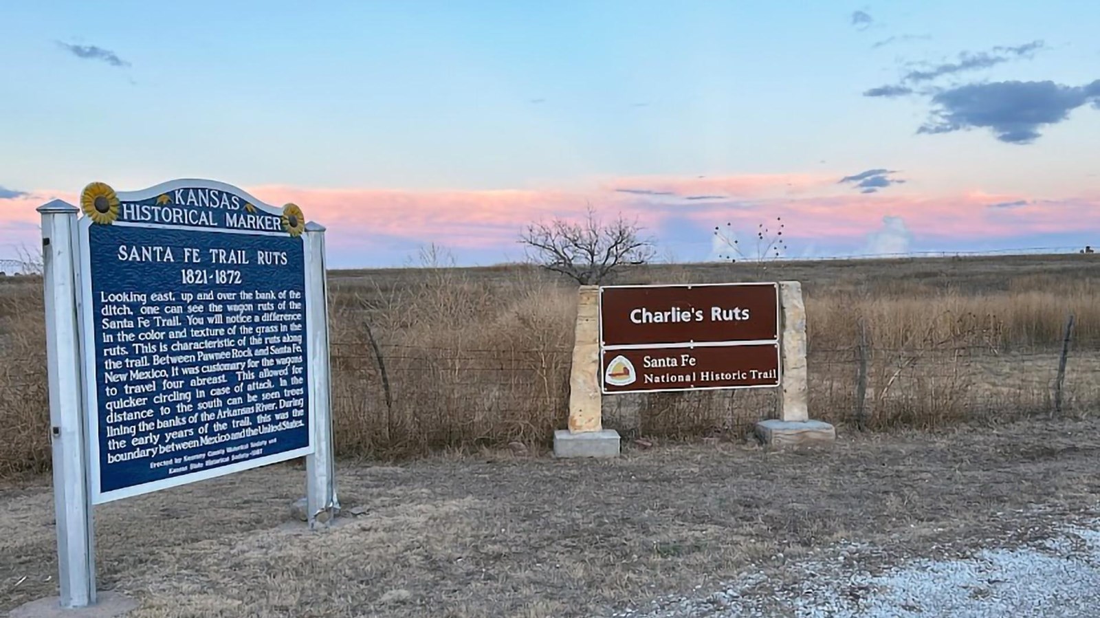 Overlooking a field are a blue Kansas Historical Marker and a brown Santa Fe Trail marker.