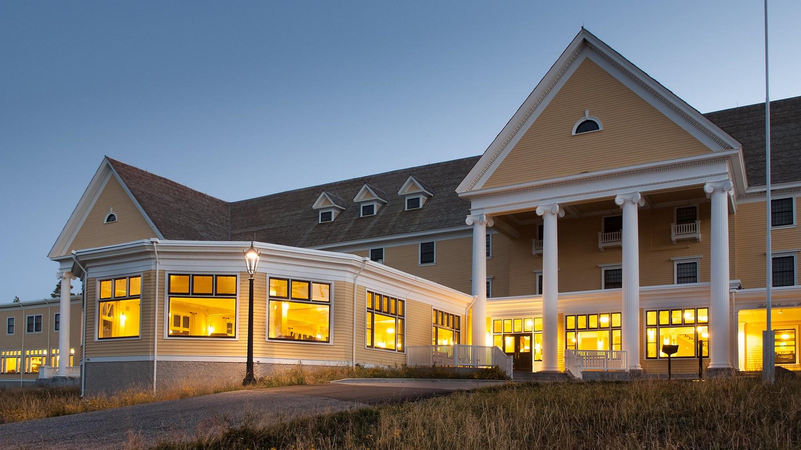 A large, grand hotel with white columns and light pouring out through the windows.