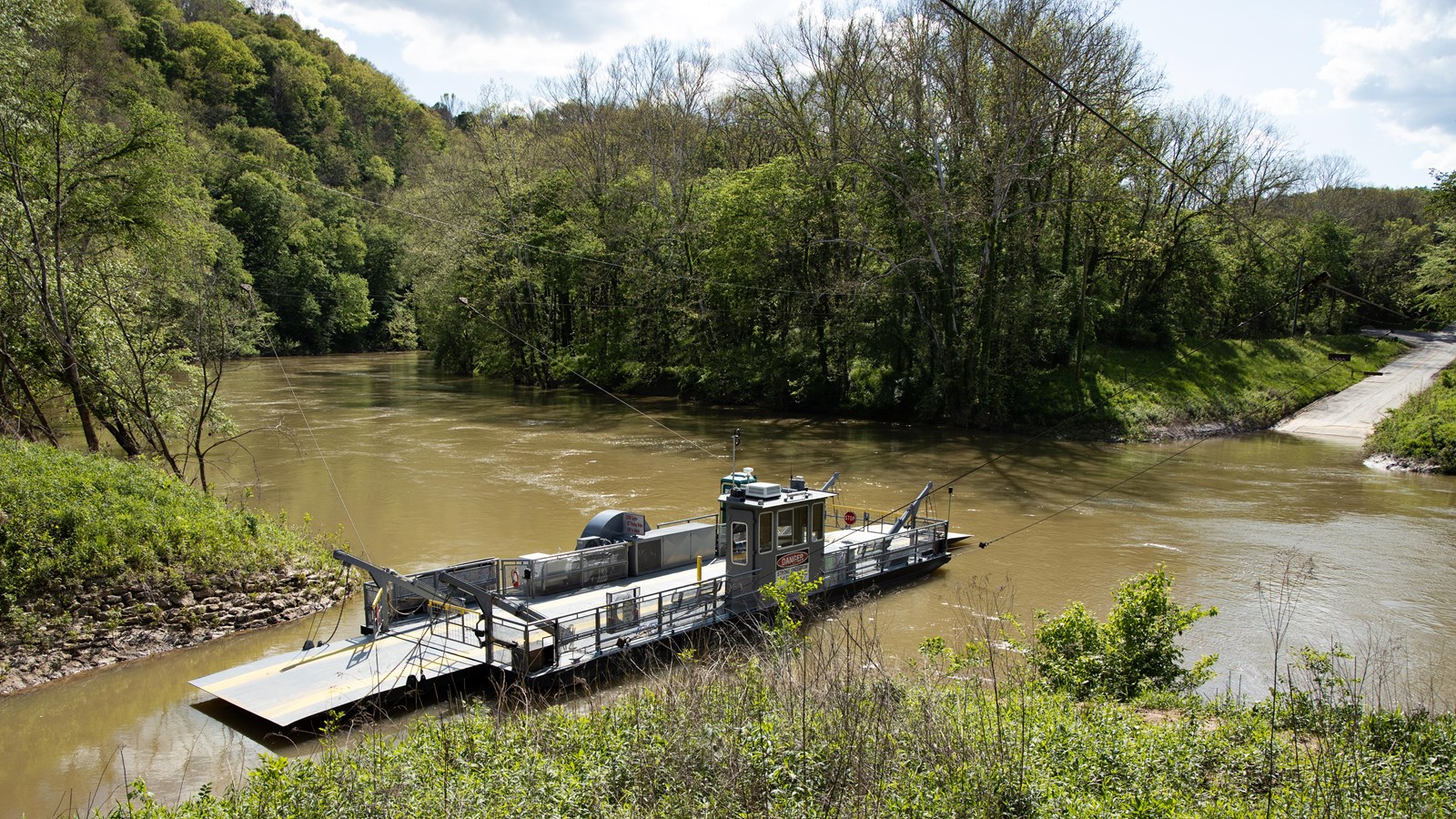 A small vehicle ferry crosses a muddy river. 