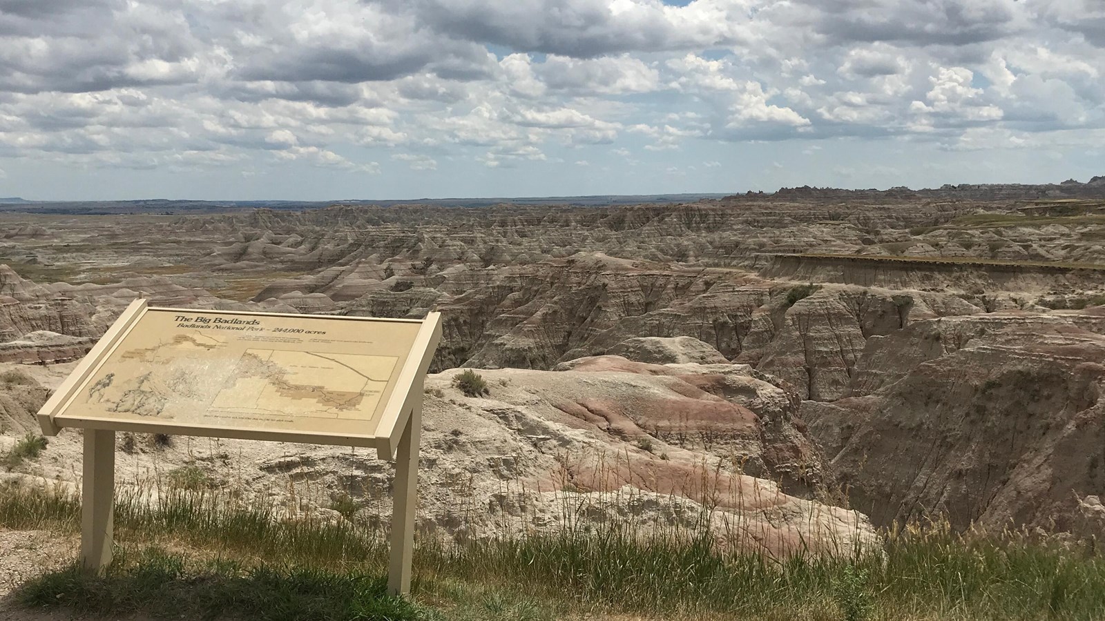 A wayside exhibit stands at the edge of drop off into badlands formations