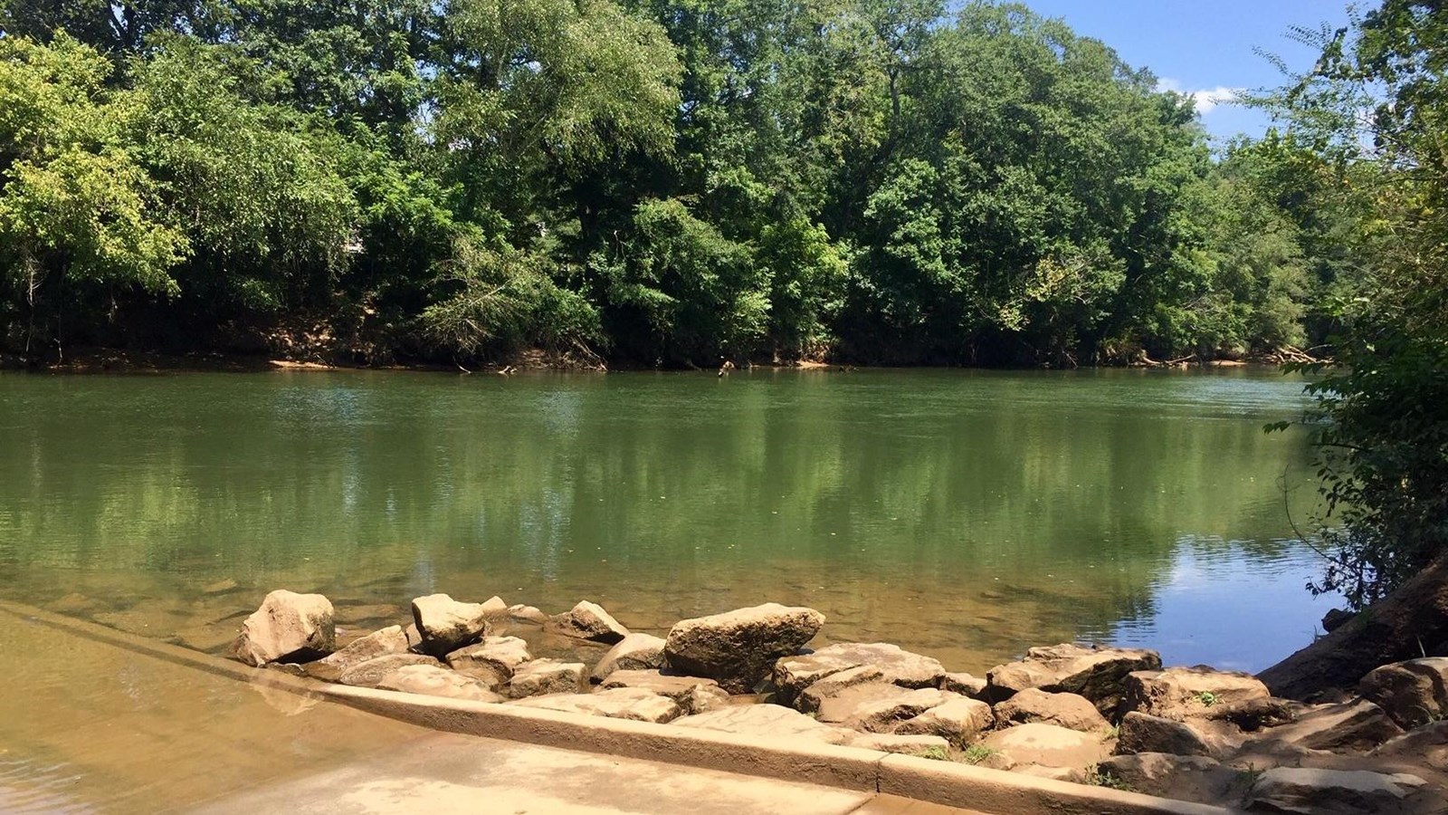 End of boat ramp as it enters the river with distant wood shoreline.