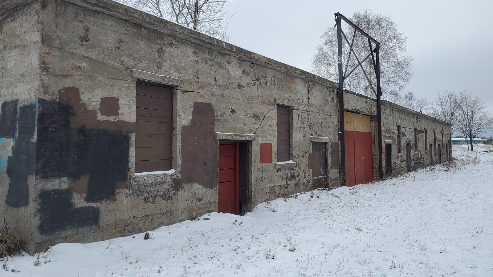 Winter scene of concrete building with boarded windows and doors.