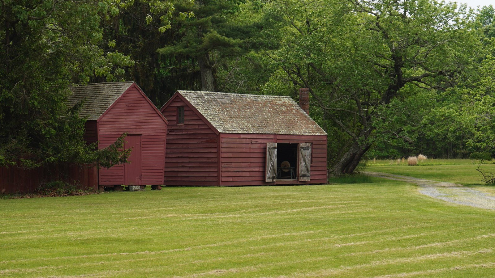 An open field features several red barnyard buildings standing on it.