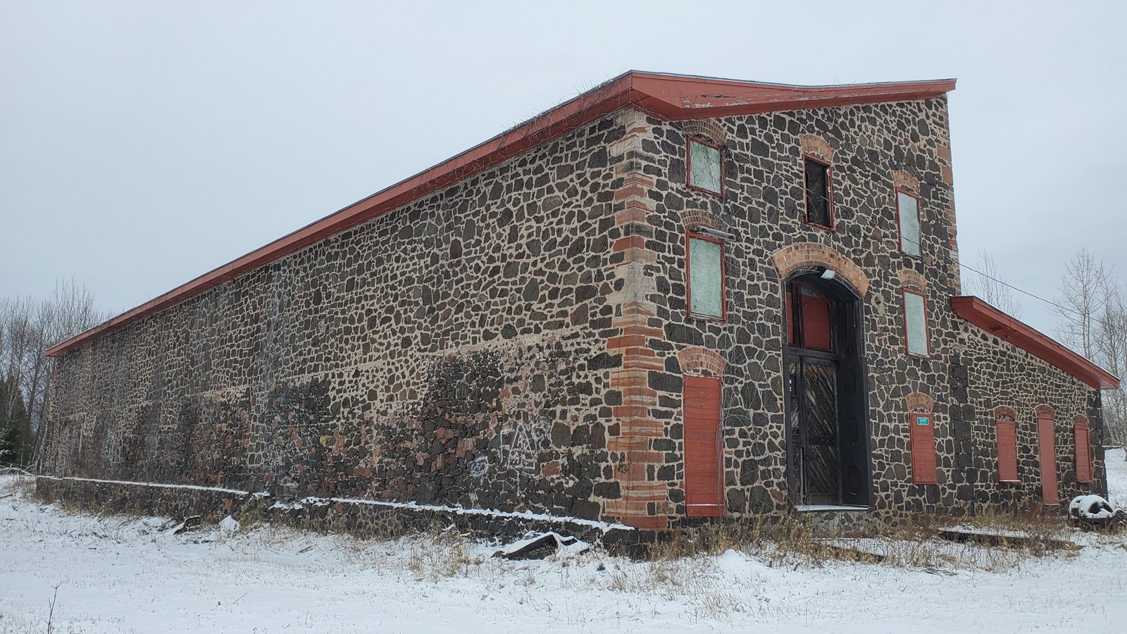 Winter scene of poor-rock two story building with red sandstone blocks on the building’s corners.