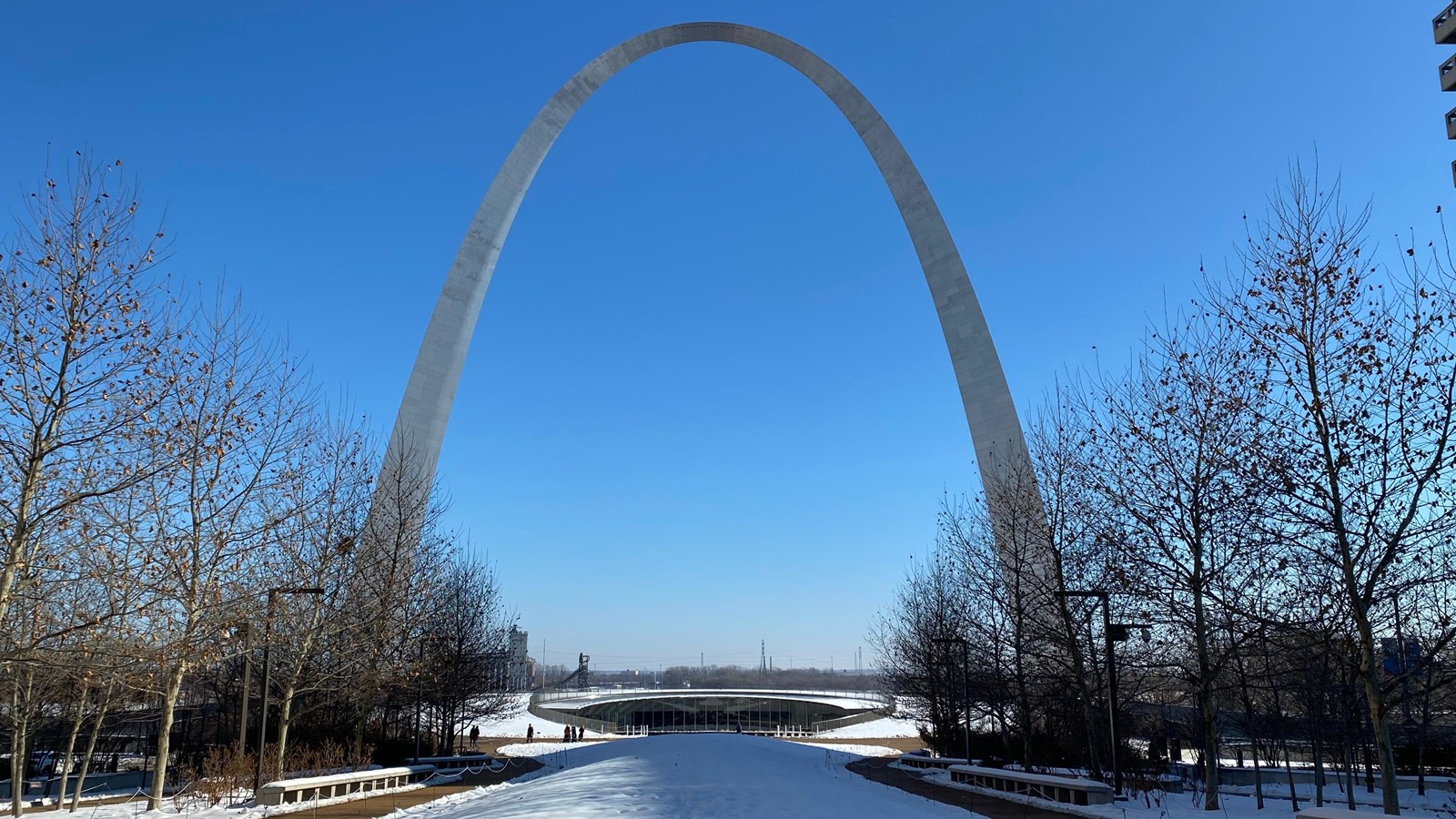 the stainless steel Gateway Arch rises 630 feet over snowy grounds against a clear blue sky