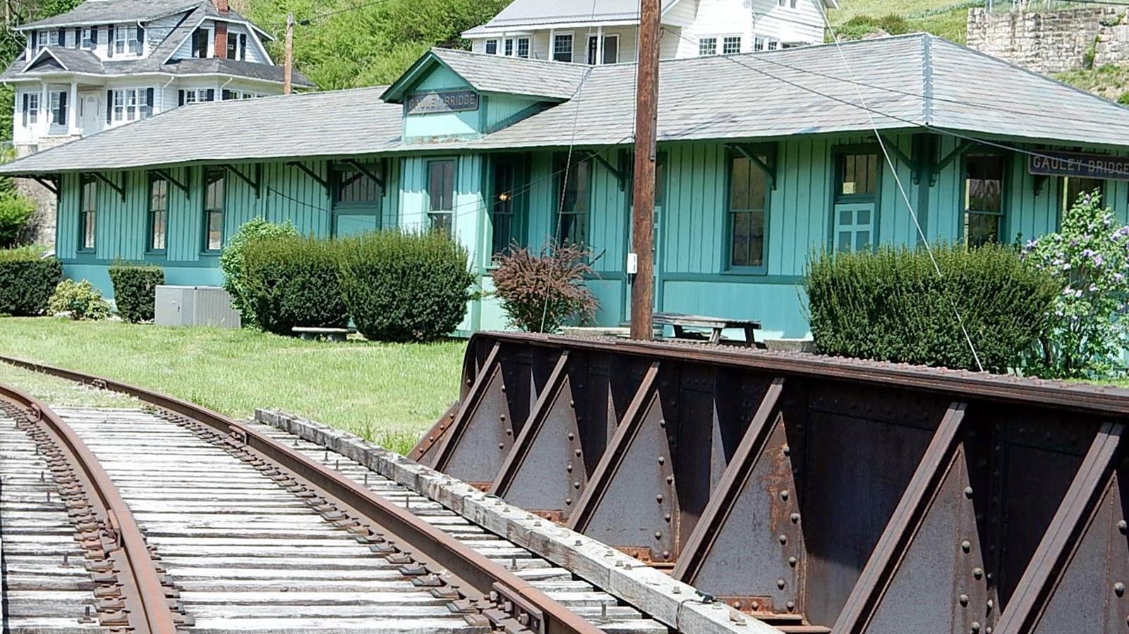 A green railroad depot with tracks in front