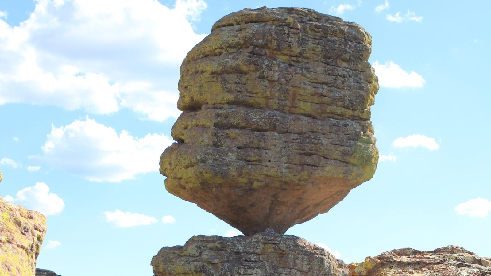 Large rock balanced on a small point against a blue and cloudy sky