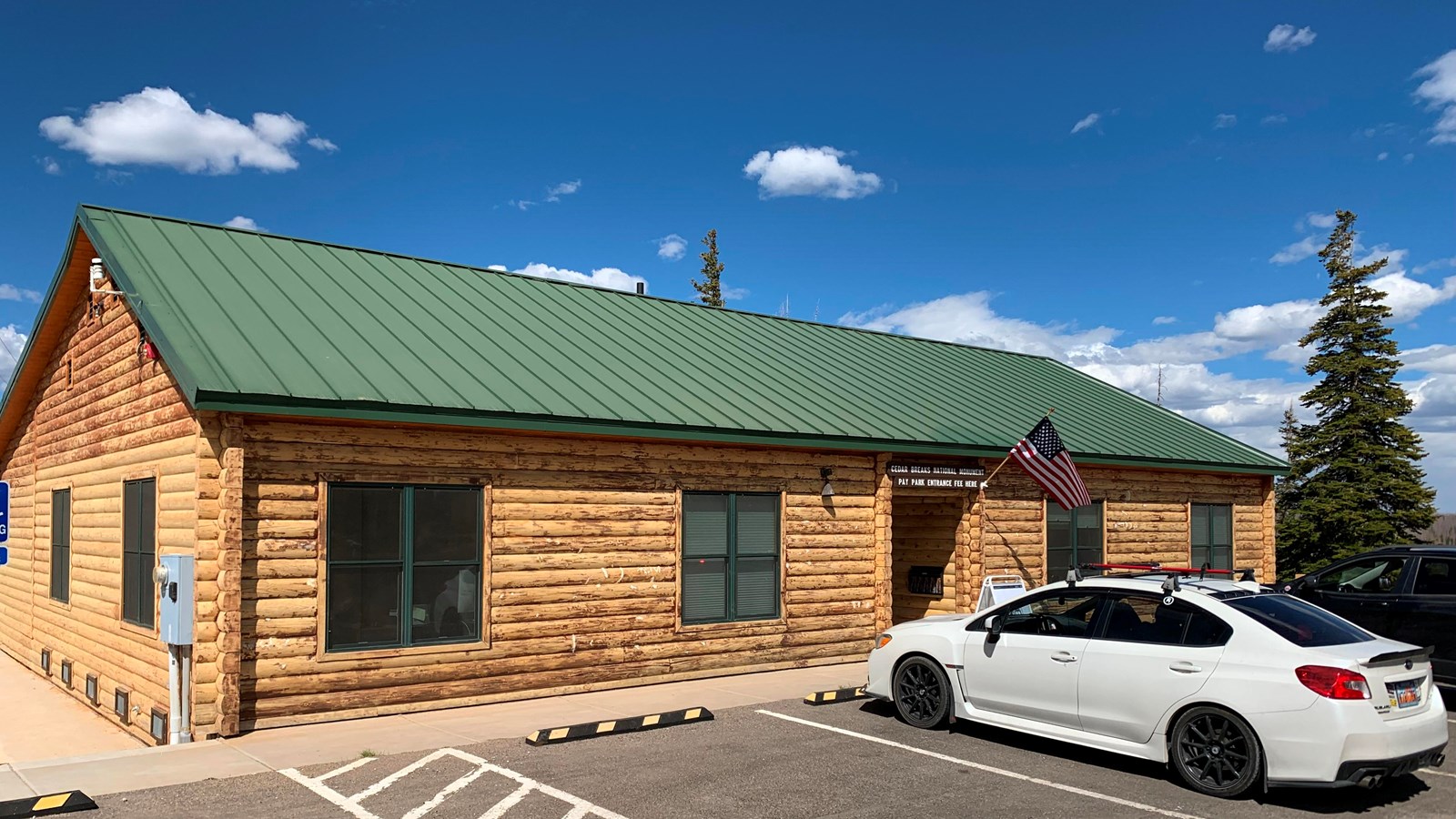 A one story log building with a green roof, cars are parked in front.