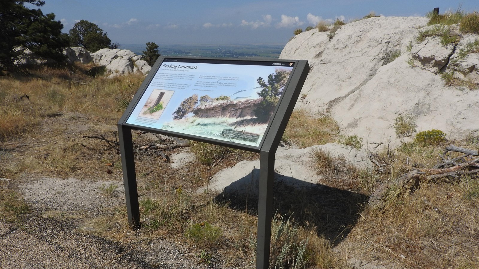 An interpretive wayside sits next to a mound of limestone with a metal post sticking out of it. 