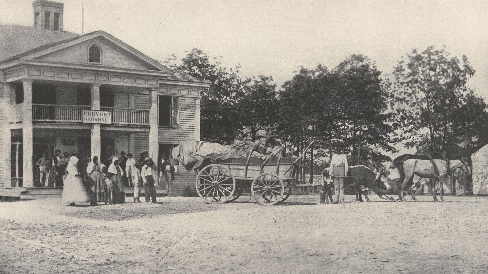 Historic image of a large building with Contraband men, wagons, and oxen in front. and wagons