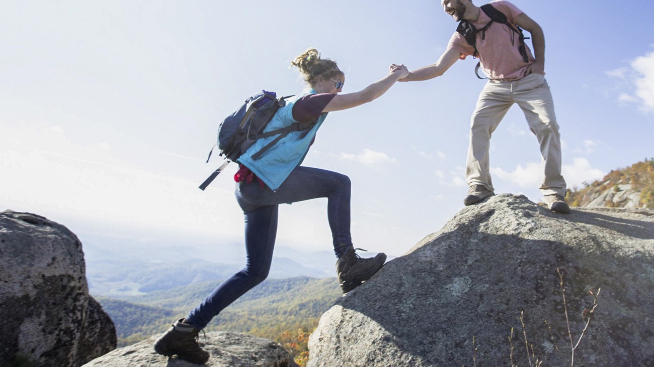 A man extends his hand on top of a rock to a woman below.