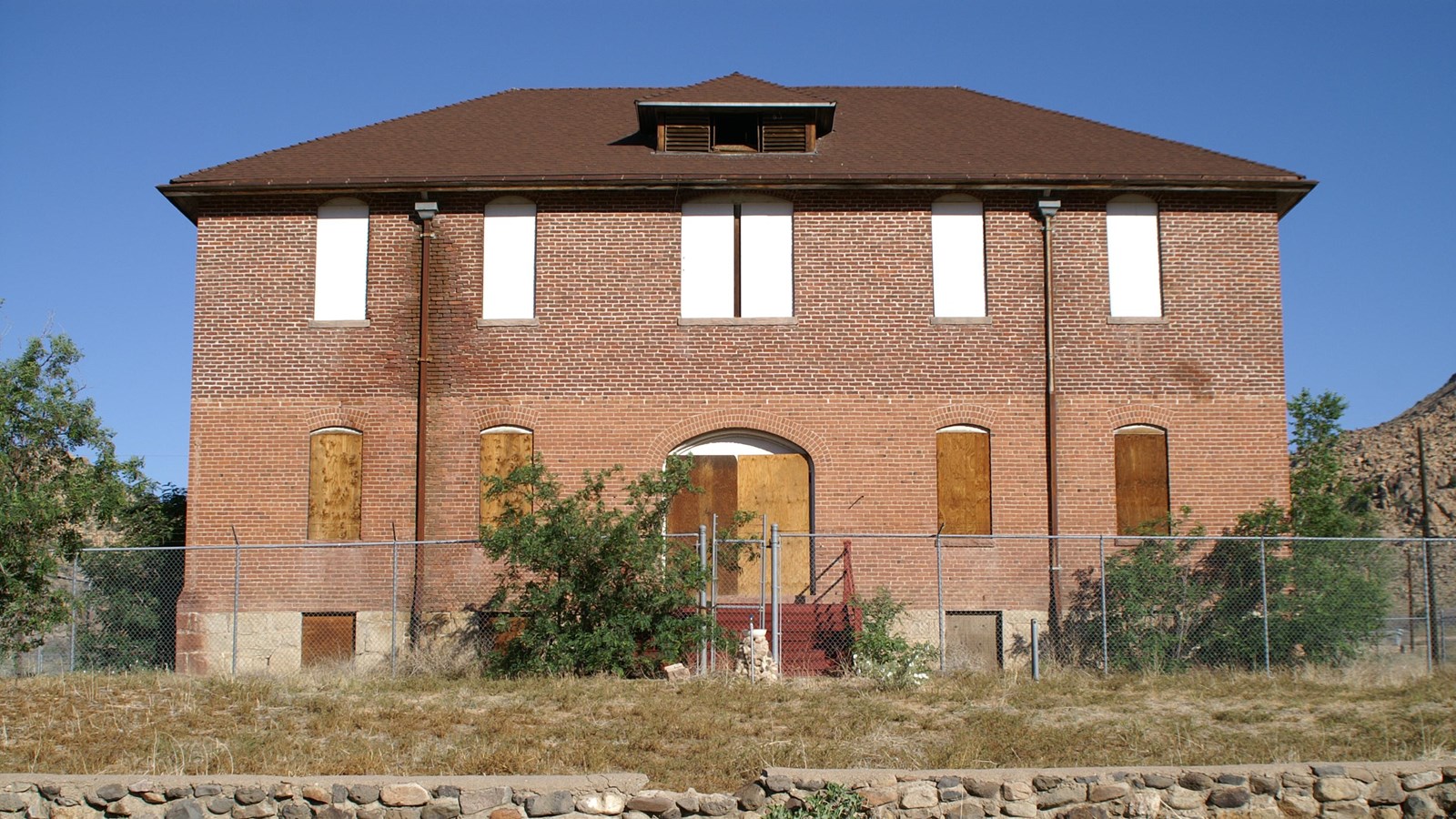 A large two story red brick building with a brown roof and boarded up windows