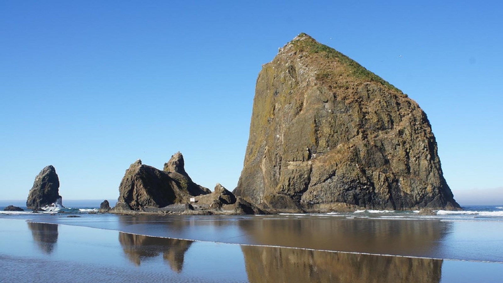 Enormous basalt rock formations rise from the shore at low tide against a blue sky