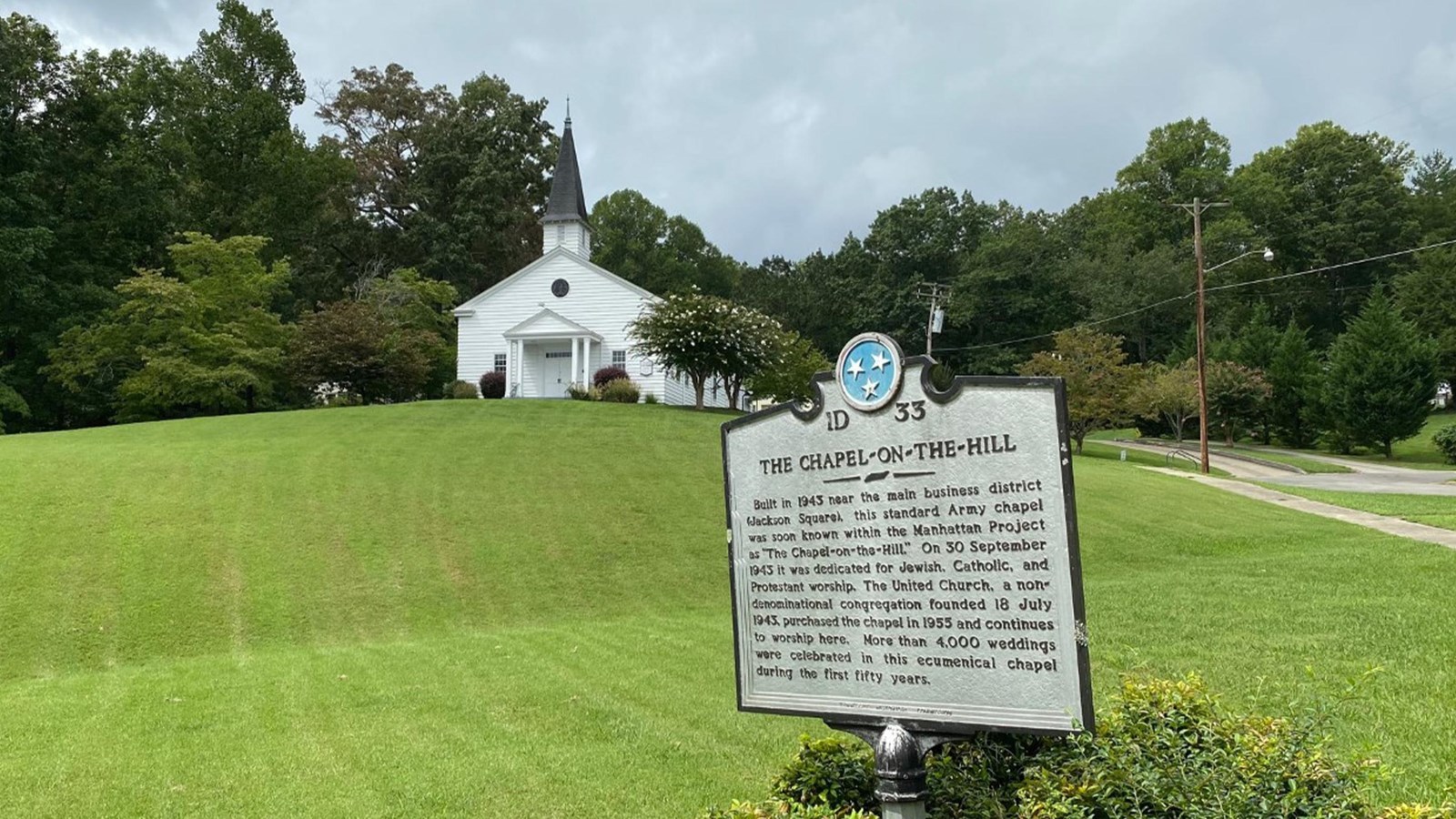 A white chapel on a grassy hill with historical marker in foreground