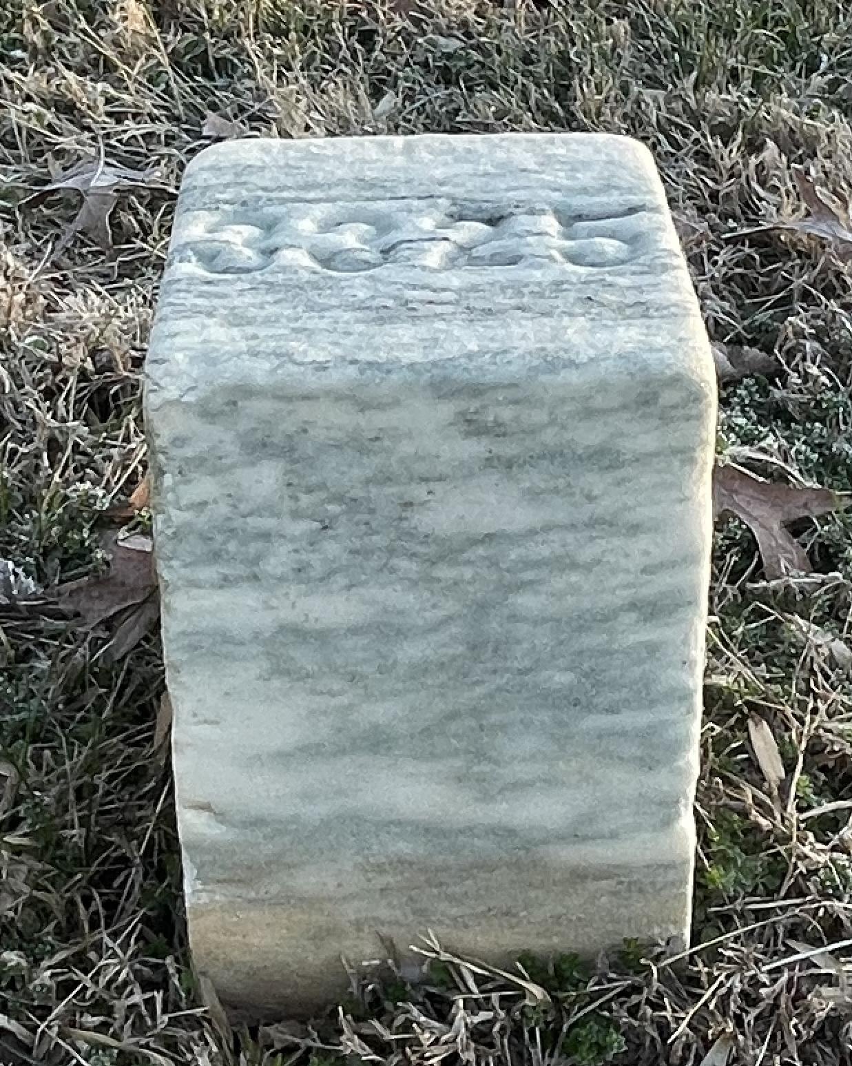 Short marble headstone with a number on the top. 