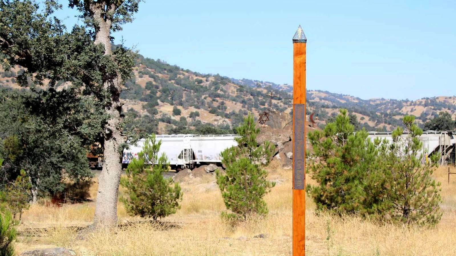 A four sided wooden pole with a metal plaque stands in a grassy field.