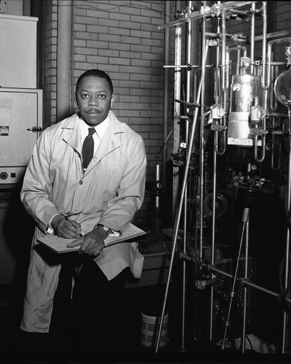 A man in a lab coat surrounded by scientific equipment.