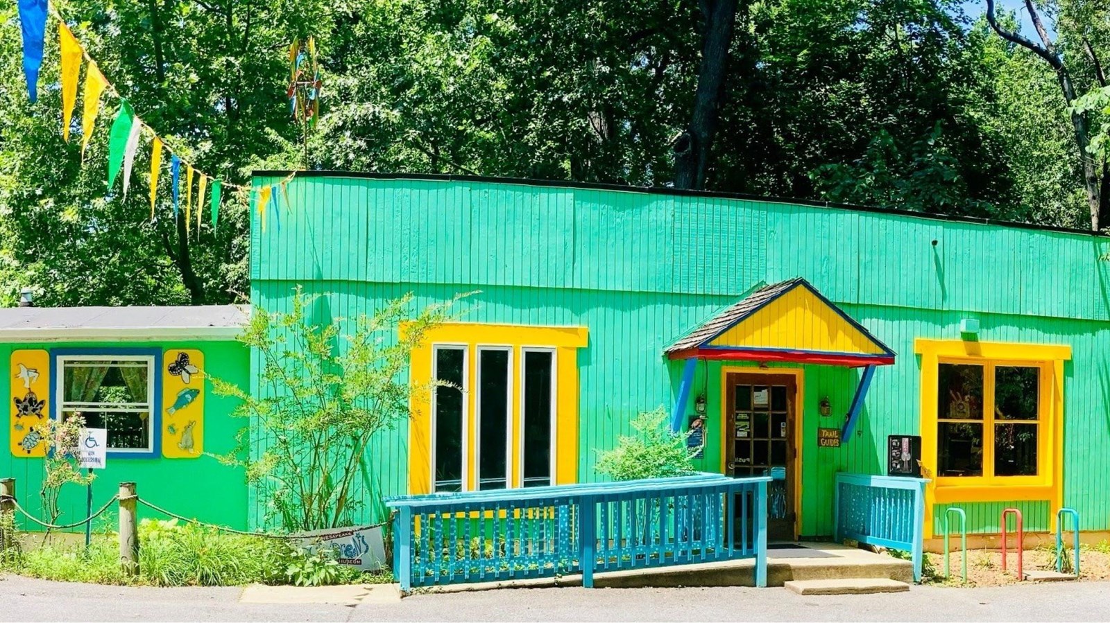 A vibrant, green building with yellow accents and colorful decorations in a wooded area.