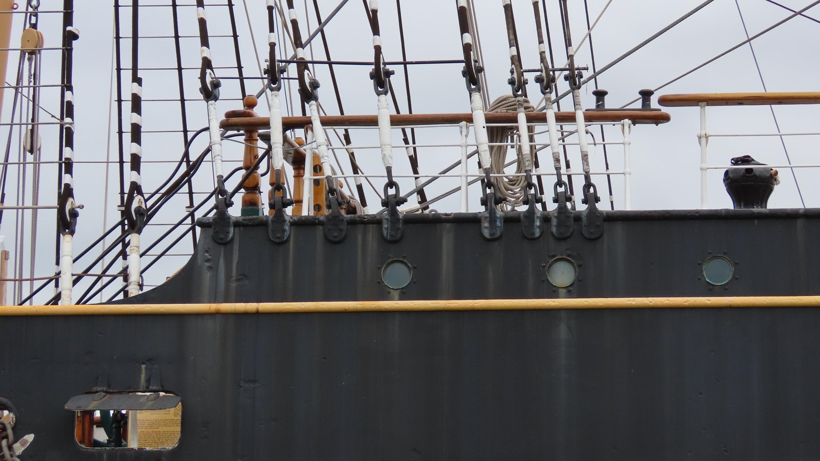A view of the poopdeck from the shore, with the deck railing, rigging, and capstan visible.