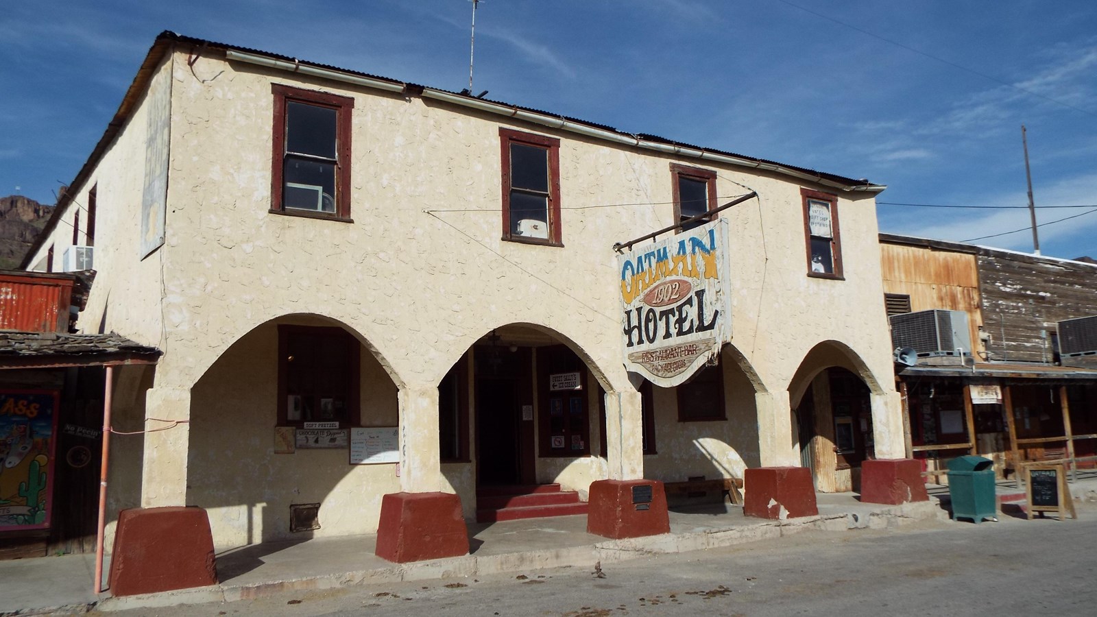 A two story white stucco building with red trim and arched doorways. A sign reads