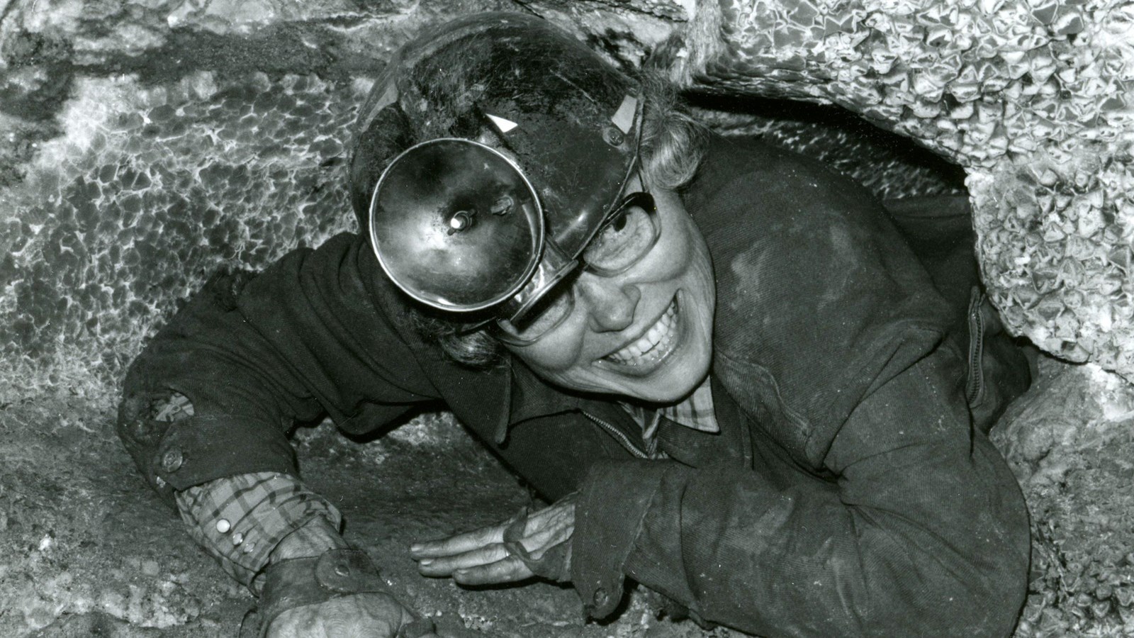 A black-and-white photo of a caver with a large headlamp. 