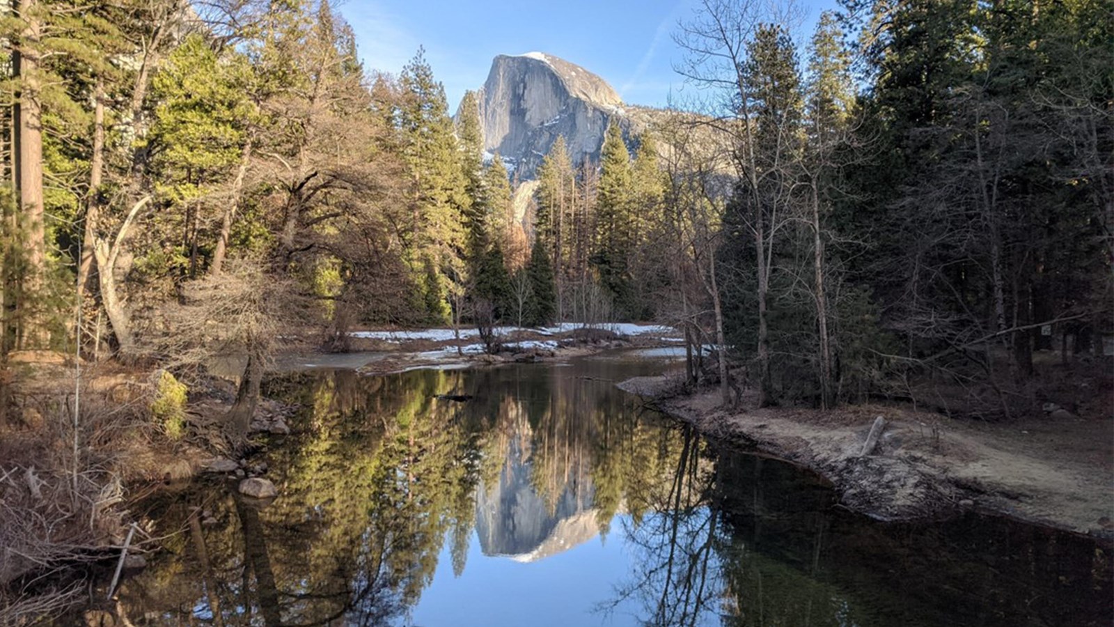A large granite formation reflects in still water surrounded by trees