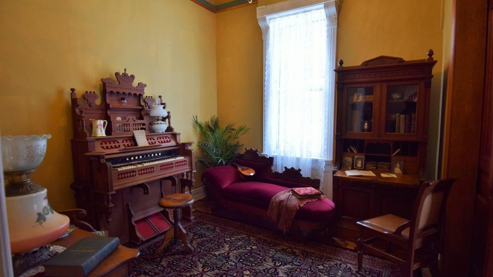 A photo of a room set to 19th century home interior with desk, loveseat, and cabinet.