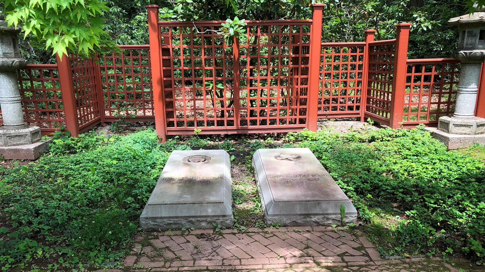 two stone slabs laying vertically side by side. A brick path, red fence and shrubs